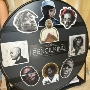 A presentation of all available stickers. These include stickers of the Pencilking artworks of Mac Miller, Tupac, The Notorious B.I.G, J.I.D, Rick Ross, Kendrick Lamar, Kempi, Hef and sticks. In the center the logo of Pencilking is seen.