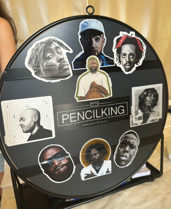 A presentation of all available stickers. These include stickers of the Pencilking artworks of Mac Miller, Tupac, The Notorious B.I.G, J.I.D, Rick Ross, Kendrick Lamar, Kempi, Hef and sticks. In the center the logo of Pencilking is seen.